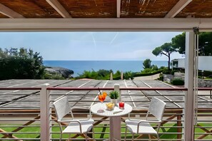 Ein überdachter Außenbereich mit Tisch, Stühlen und Blick aufs Meer.