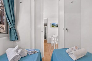 Een hotelkamer met twee bedden, een raam met gordijnen, een tafel met een tijdschrift en een schilderij aan de muur.