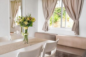 Ein Essbereich mit einem Tisch, Stühlen, einer Blumenvase und Blick durch das Fenster.