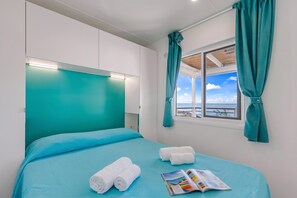 Ein Hotelzimmer mit einem Bett, einem Fenster mit Vorhängen und Blick aufs Meer.