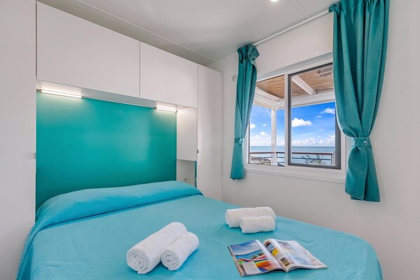 Une chambre d’hôtel avec un lit, une fenêtre avec des rideaux et une vue sur la mer.