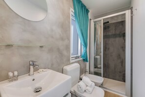 Ein Badezimmer mit Waschbecken in Weiß, Toilette, Dusche mit Glastür und einem türkisfarbenen Duschvorhang.
