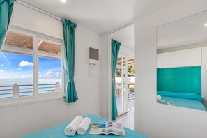 A room with a bed, a window with curtains, a view of the sea, and a small table with a magazine. - Sea View - 40 Parallelo - Deluxe 5, Marina di Camerota, Italy (Marina di Camerota)