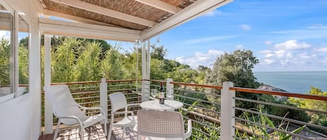 A covered outdoor seating area with a table and chairs, overlooking a scenic landscape.