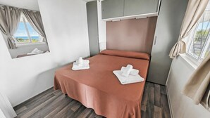 A single bed with a brown bedspread and two white towels, a window with curtains, and a view of the outdoors. - Sea View - 40 Parallelo - Deluxe 5, Marina di Camerota, Italy (Marina di Camerota)