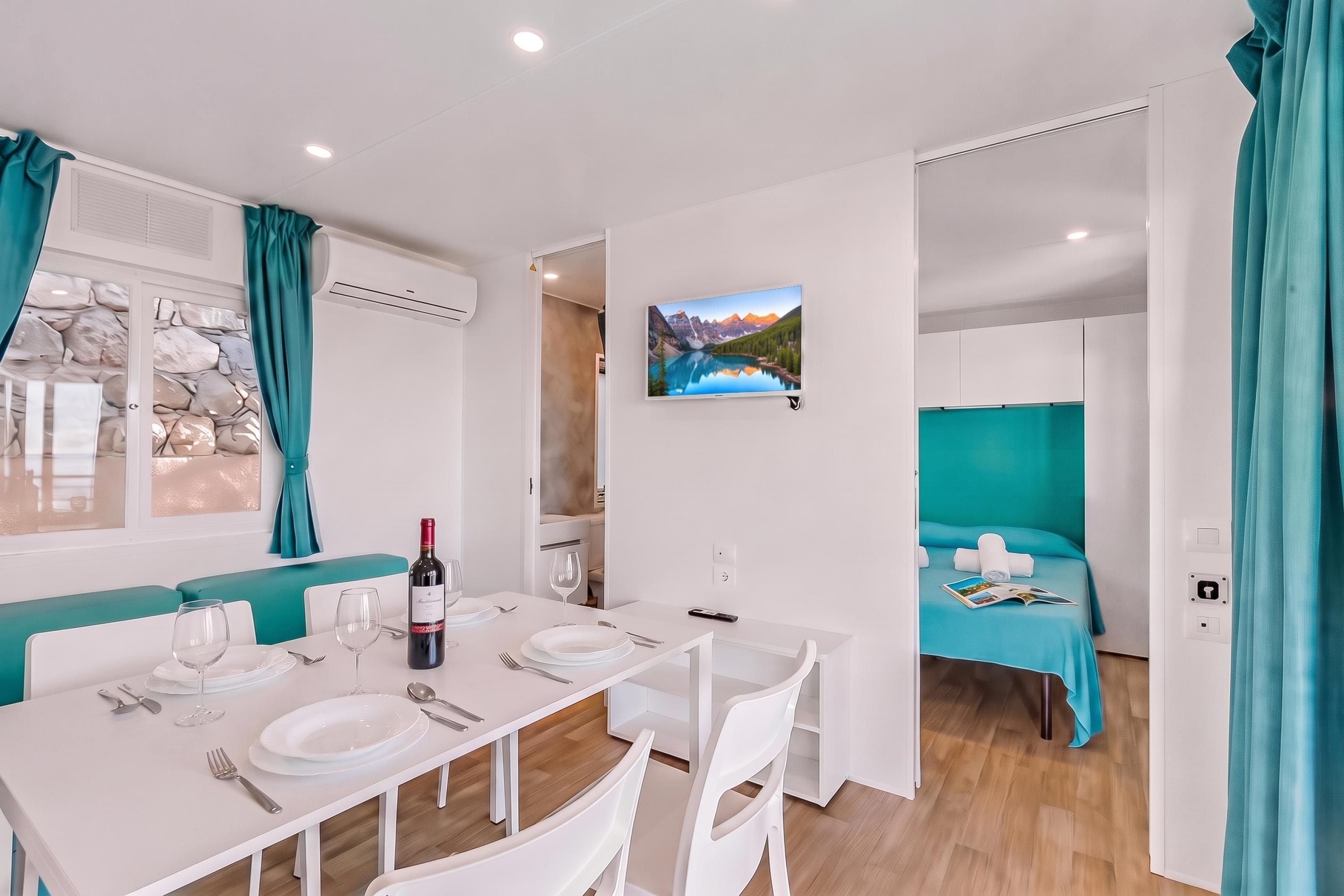 Une chambre d’hôtel moderne avec un coin repas, un lit doté d’une tête de lit bleue, un tableau représentant un paysage de montagne et une vue sur un mur rocheux.