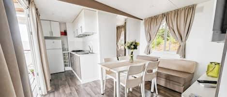 Una cocina compacta con armarios blancos, un área de comedor con mesa y sillas, y una sala de estar con sofá y televisor.