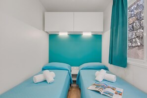 A small, modern room with two single beds, a teal-colored wall, a window with a curtain, and a magazine on the bed. - Sea View - 40 Parallelo - Deluxe 5, Marina di Camerota, Italy (Marina di Camerota)