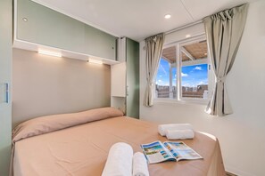 Een hotelkamer met een bed, een raam met gordijnen, een nachtkastje met een tijdschrift en een wandlamp.