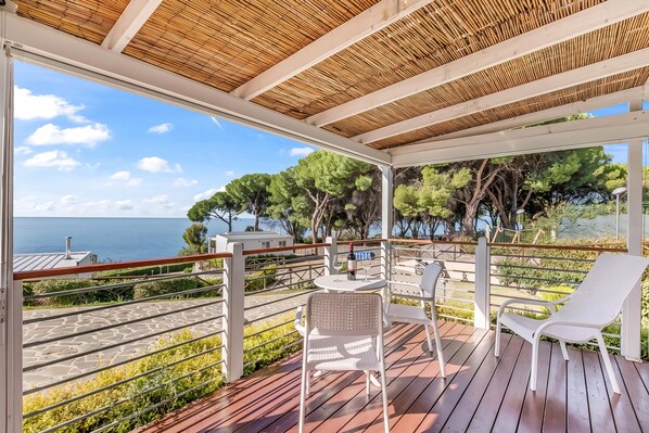 A covered outdoor seating area with a view of the sea and trees.