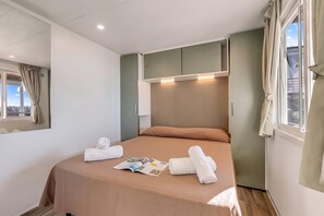 A hotel room with a bed, a window with curtains, a bedside table, and a magazine.
