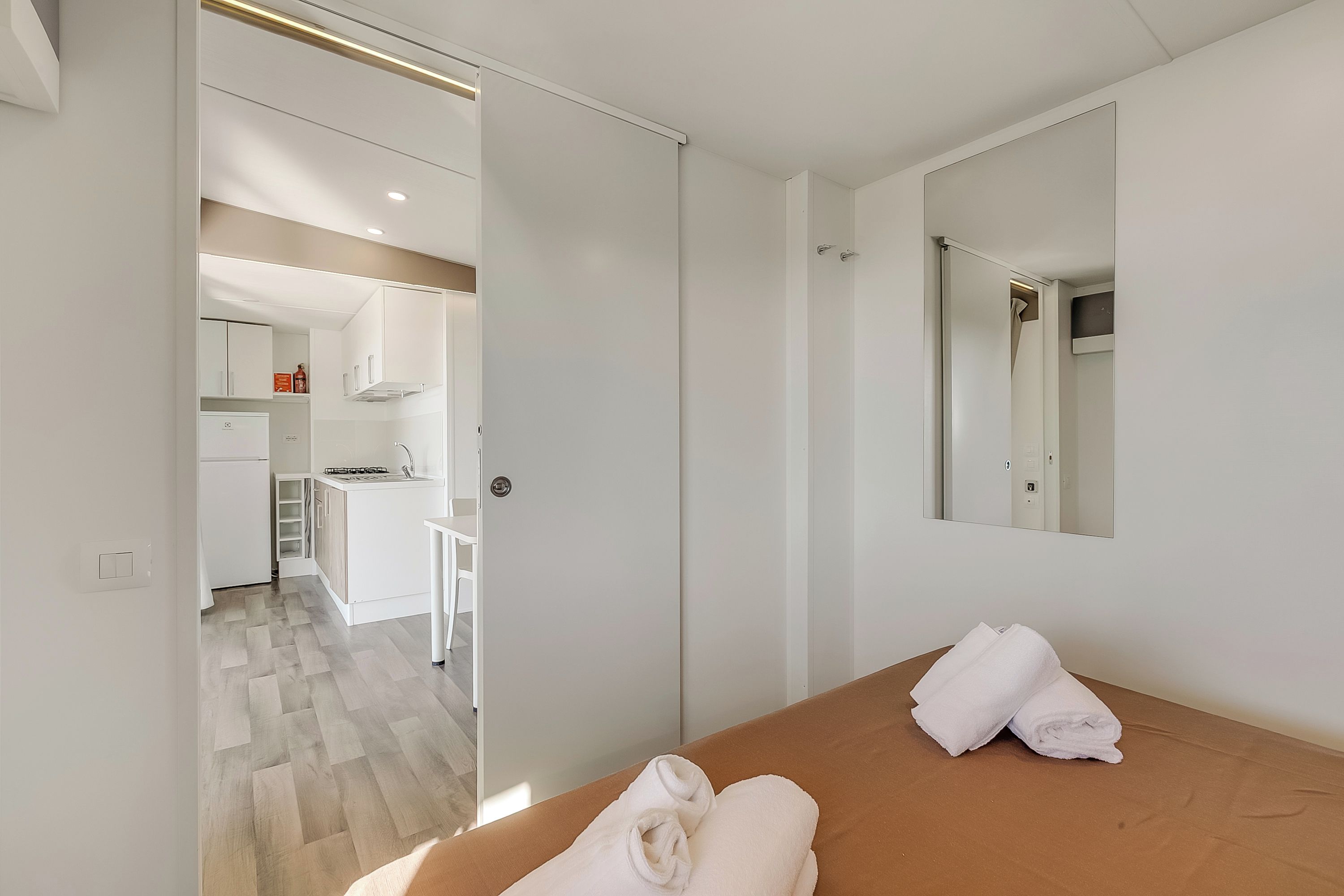 Een hotelkamer met een bed, een badkamer en een keukenruimte, zichtbaar door een open deur.