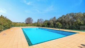 En rektangulär swimmingpool med en kakelbeklädd poolkant, omgiven av träd och ett staket.