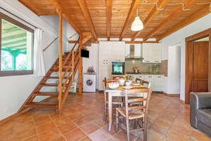 Une cuisine avec des meubles blancs, une table à manger avec des chaises, un escalier en bois et un lave-linge.