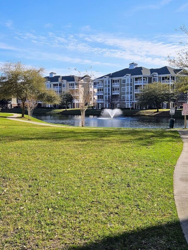 A building with a large lawn, a fountain, and a body of water. - Sweet Magnolias | Beach Escape Near Top Courses (Myrtle Beach)