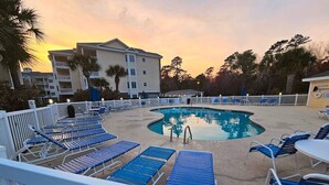 A pool area with blue lounge chairs, a pool, and a building in the background. - Sweet Magnolias | Beach Escape Near Top Courses (Myrtle Beach)