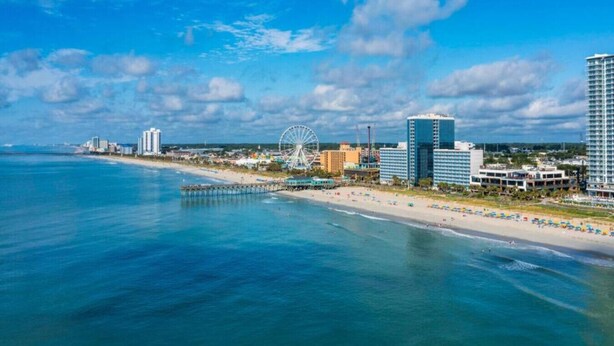 A coastal cityscape with a beach, a large Ferris wheel, and high-rise buildings. - Sweet Magnolias | Beach Escape Near Top Courses (Myrtle Beach)