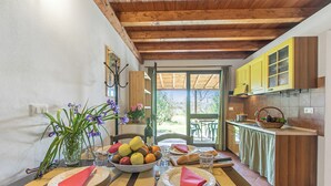 Un comedor con una mesa de madera dispuesta para dos personas, un cuenco de fruta y un jarrón de flores.