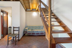 Uma escada de madeira, uma cadeira de madeira, um sofá estampado e um chão de azulejos.