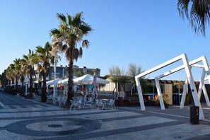 Ein gepflasterter Außenbereich mit Palmen, Sitzgelegenheiten im Freien und einem modernen Gebäude im Hintergrund.