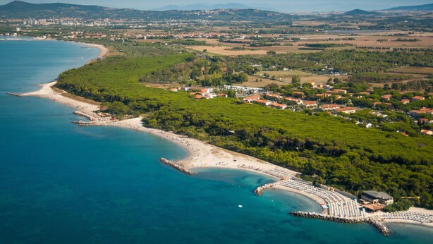 Vista aérea de un pueblo costero con playa, zonas verdes y un mar azul y despejado.