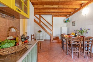 Una cocina con una escalera de madera, un área de comedor con sillas y un televisor montado en la pared.