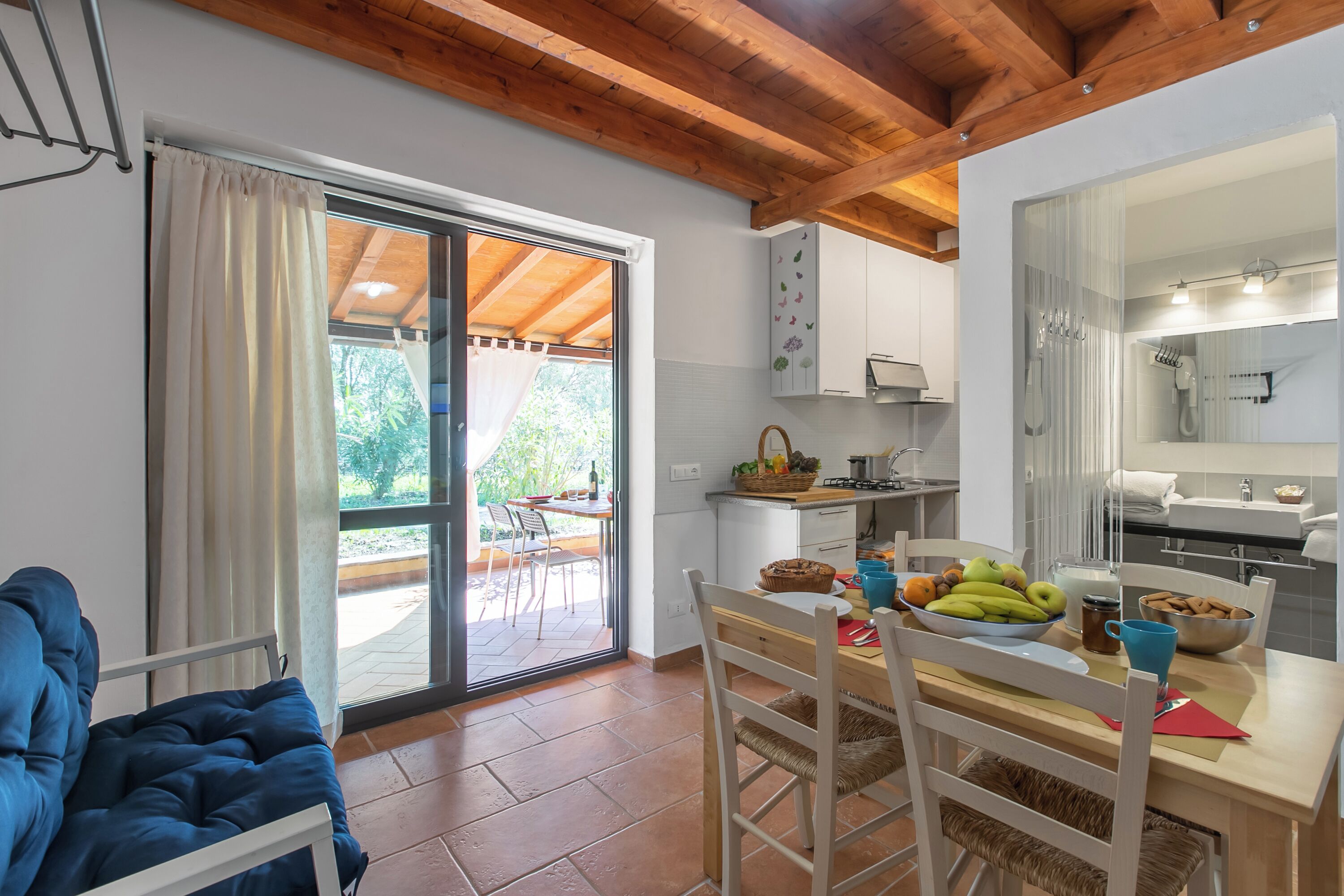 A cozy kitchen with a dining area, wooden ceiling beams, and a sliding glass door leading to an outdoor patio.