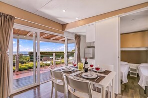 Un coin repas avec une table dressée pour deux personnes, une bouteille de vin et une vue sur l’extérieur.