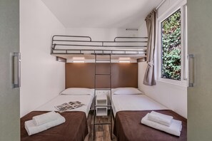 Een slaapkamer met stapelbed, een ladder, twee bedden, een raam met gordijnen en een klein tafeltje met een tijdschrift.