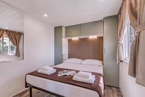 Une chambre d’hôtel avec un lit, une table de chevet, une fenêtre avec des rideaux et un luminaire fixé au mur.