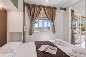 A hotel room with a bed, a window with curtains, a view of the outdoors, and a magazine on the bed. - Sea View - 40 Parallelo - Deluxe 1, Marina di Camerota, Italy (Marina di Camerota)