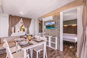 A compact living space with a dining area, a TV mounted on a wall, and a bed with a wooden panel design. - Sea View - 40 Parallelo - Deluxe 1, Marina di Camerota, Italy (Marina di Camerota)