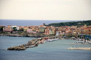 Une ville côtière aux bâtiments aux couleurs vives, un port de plaisance avec des bateaux et une digue rocheuse.