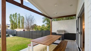 A patio with a wooden table and benches, a grill, and a view of the backyard. - Lakeshore Serenity @ Warners Bay (Warners Bay)