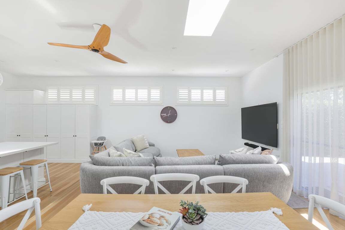 Een moderne woonkamer met een bank, televisie, plafondventilator en eethoek.