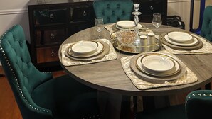 Comedor con mesa redonda para cuatro personas, una araña y decoración en la pared.