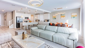 Una cocina moderna con armarios blancos, una isla central y una zona de comedor con sillas color naranja.