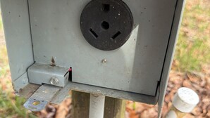 A utility box with a circular opening, a metal plate with holes, and a white pipe.