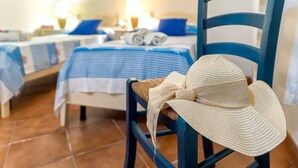 Una camera d'albergo con due letti, una sedia con un cappello di paglia e un comodino con una lampada.