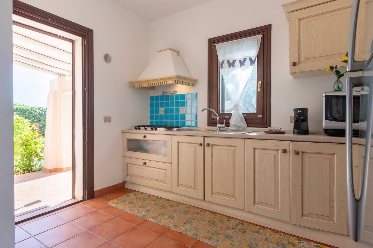 A kitchen with a stove, sink, cabinets, and a window with curtains.