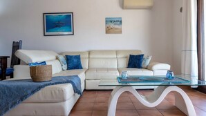 Un soggiorno con un divano beige, un tavolino in vetro e un quadro di uno squalo appeso al muro.