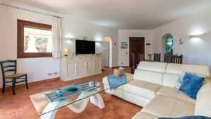 Un soggiorno con divano, tavolino in vetro, televisione su un mobile e zona pranzo con sedie e tavolo.