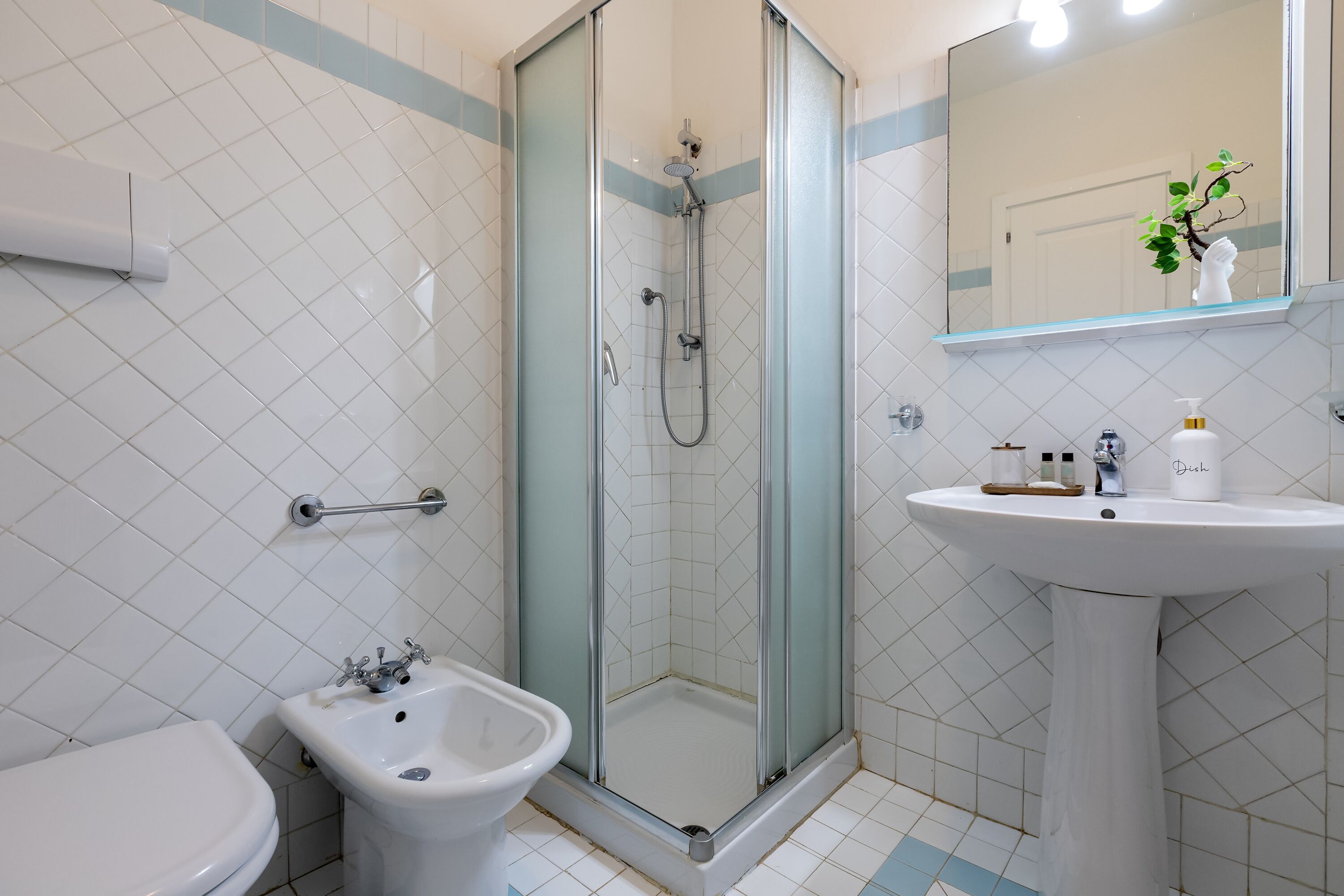 Un baño con ducha de mampara, lavamanos sobre pedestal y inodoro.