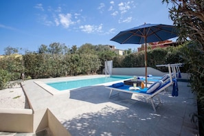 A swimming pool with lounge chairs and an umbrella, surrounded by greenery and a clear sky. - Villa Aquamarina - Private Pool (Stintino)