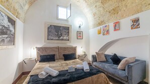 Une chambre à coucher avec un lit, un canapé, une table de chevet, une lampe et un tableau encadré au mur.