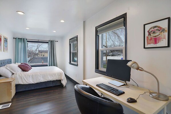 Una habitación de hotel moderna con cama, escritorio, computadora y ventanas amplias.