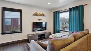 A living room with a flat-screen TV, a sofa, a coffee table, and a window with curtains. - Private patio, close to downtown & all major ski resorts (South Salt Lake)