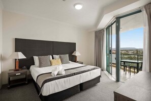 Un cuarto de hotel con una cama grande, dos mesitas de noche, un balcón con una mesa y vistas al paisaje.