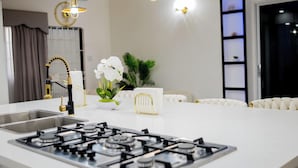 Une cuisine moderne équipée d’une cuisinière à gaz, d’un évier en acier inoxydable et de luminaires suspendus.