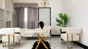 Un salon moderne comprenant un canapé, deux fauteuils, une table basse en verre et un vase décoratif.